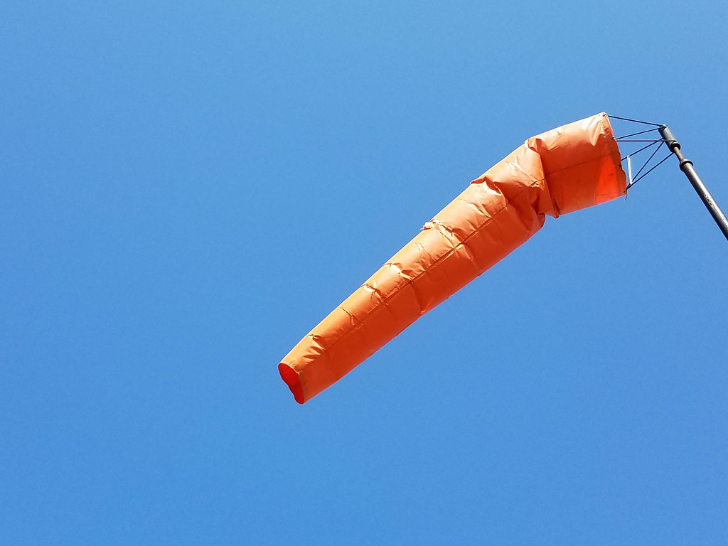 An airport windsock extended in a strong crosswind beside a runway